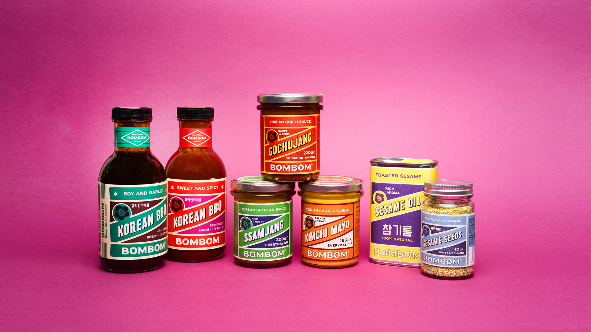 Korean condiment bottles and jars with BOMBOM labels grouped together on a pink background.