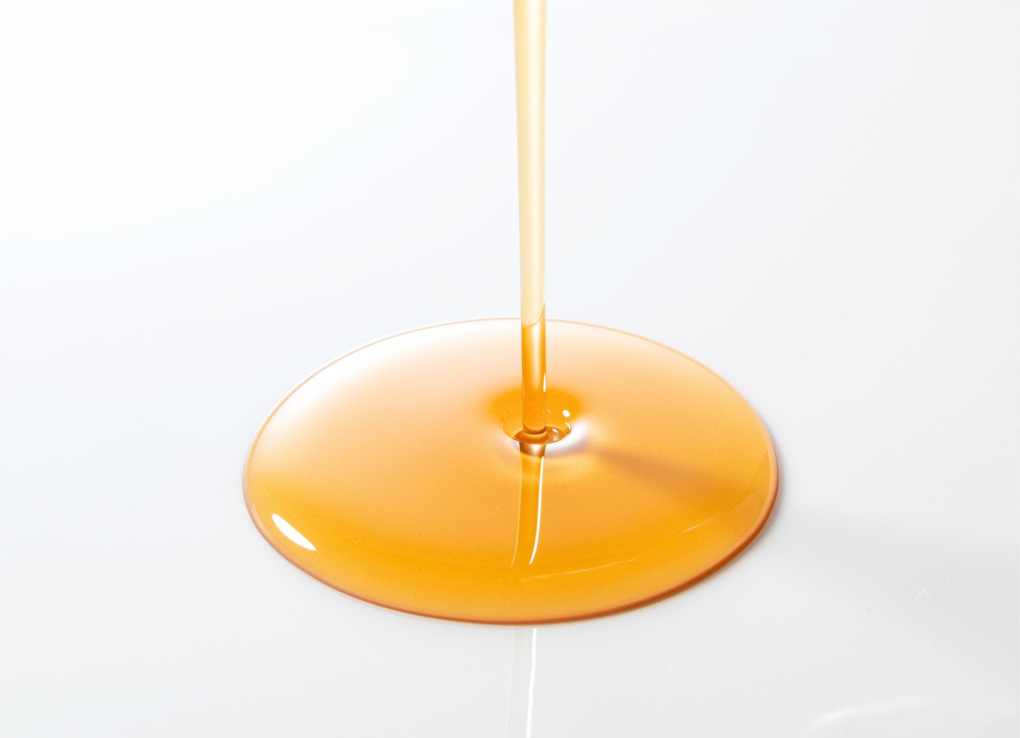 Korean BOMBOM amber liquid puddle with a thin stream and glossy dome-shaped surface on white background